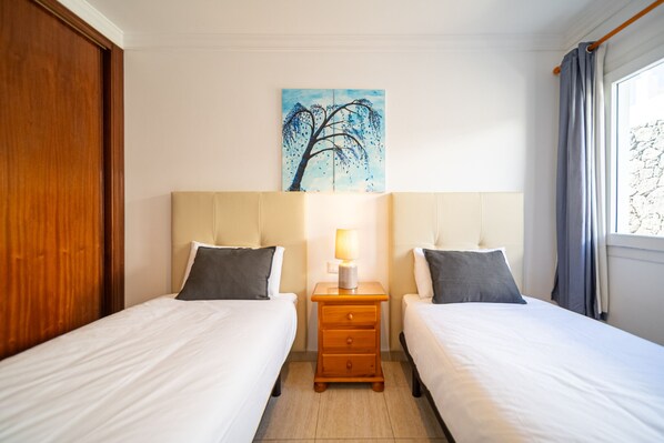 Una habitación de hotel con dos camas, una mesita de noche con lámpara y un cuadro de un árbol en la pared.