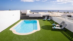 En pool på taket med fri utsikt över havet, omgiven av vita väggar och en stenmur.