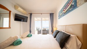 Ett hotellrum med en stor säng, en platt-TV, en tavla på väggen och utsikt över omgivningarna genom dörren.