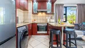 Eine kompakte Küche mit Backofen von Bosch, einer Waschmaschine und einer Essecke mit Barhocker.