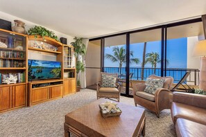 A living room with a television, bookshelves, and a view of the ocean. - Oceanfront 1BR in Kihei w/ lanai and pool access (Kihei)