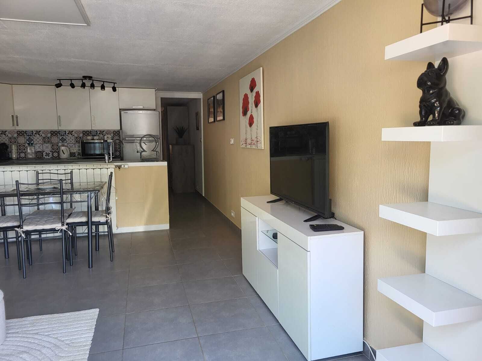 A modern kitchen with a dining area, a flat-screen TV, and a small statue on a shelf.