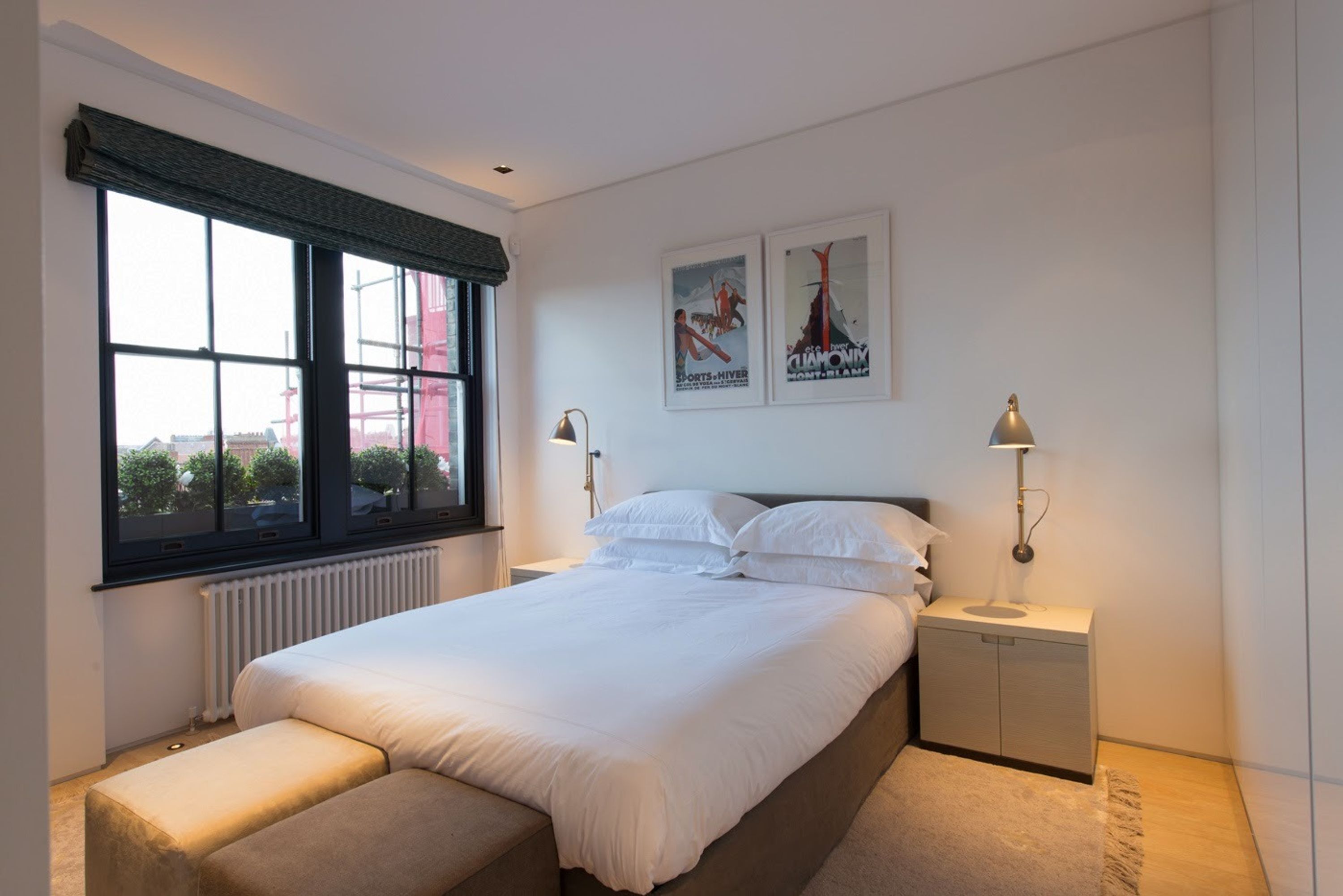 Una camera da letto con un'ampia finestra, un letto, un comodino e una panca.