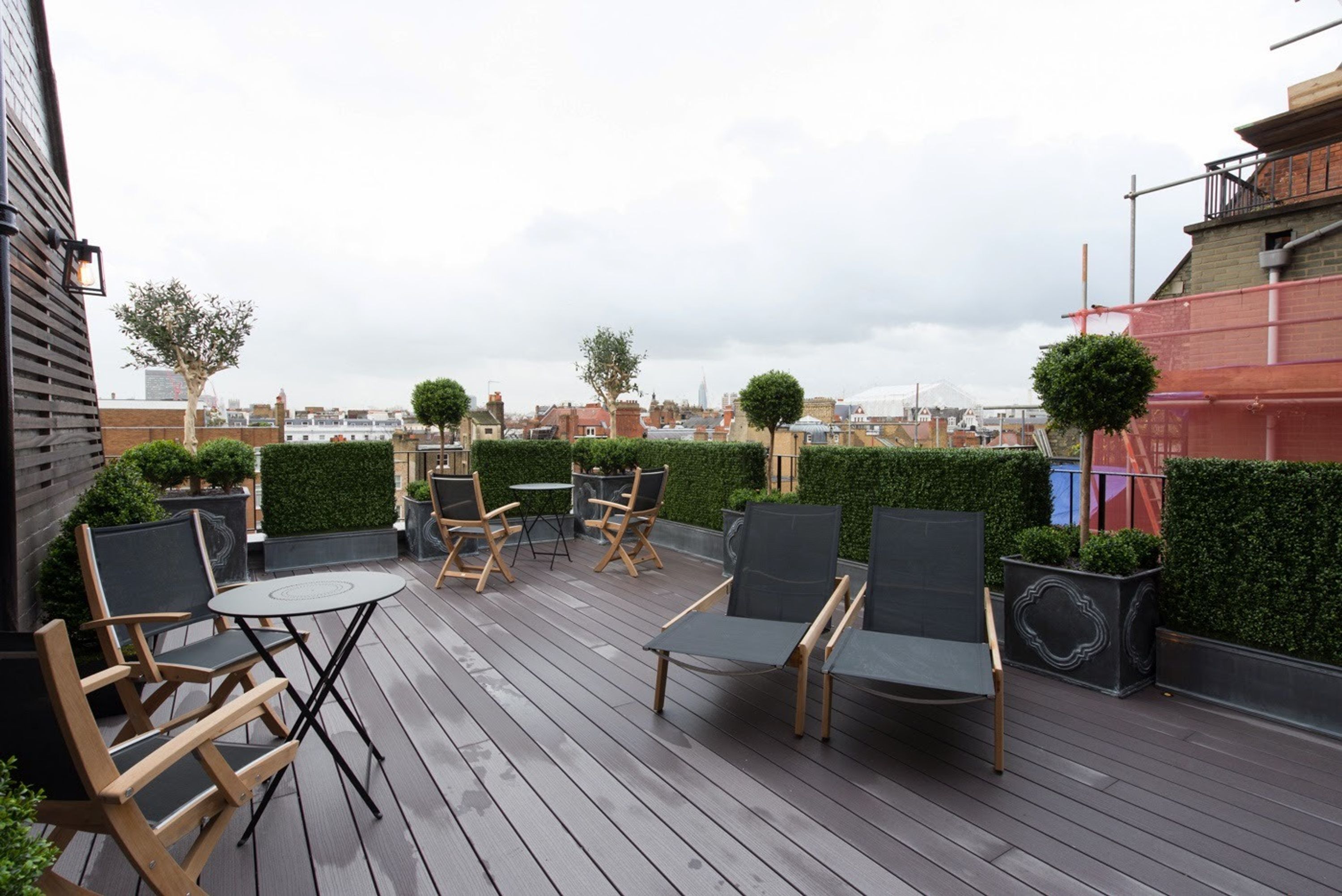 A rooftop terrace with wooden flooring, multiple seating areas, and green hedges.