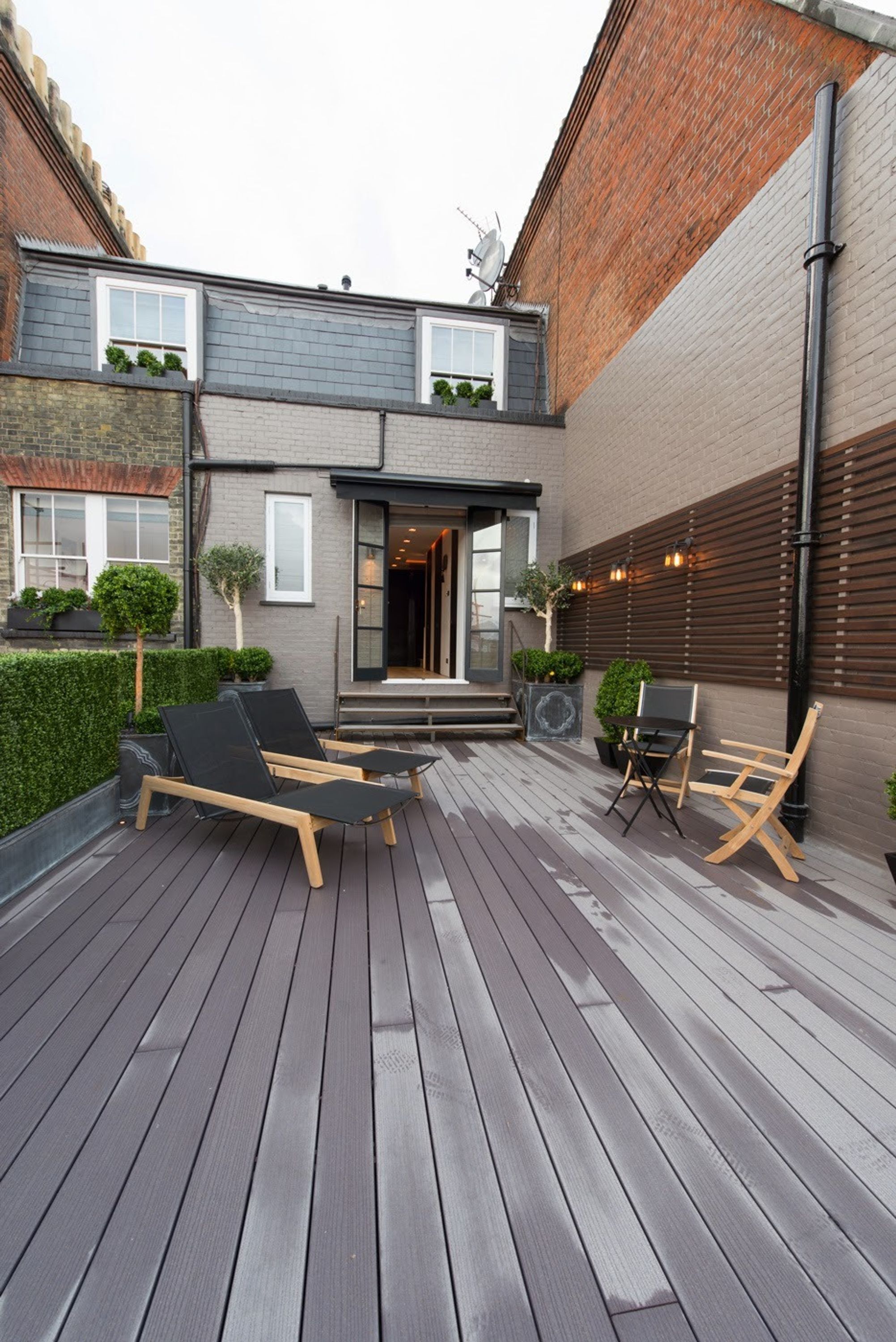 Un patio moderne avec un plancher en bois, deux fauteuils, une petite table et des plantes en pot.