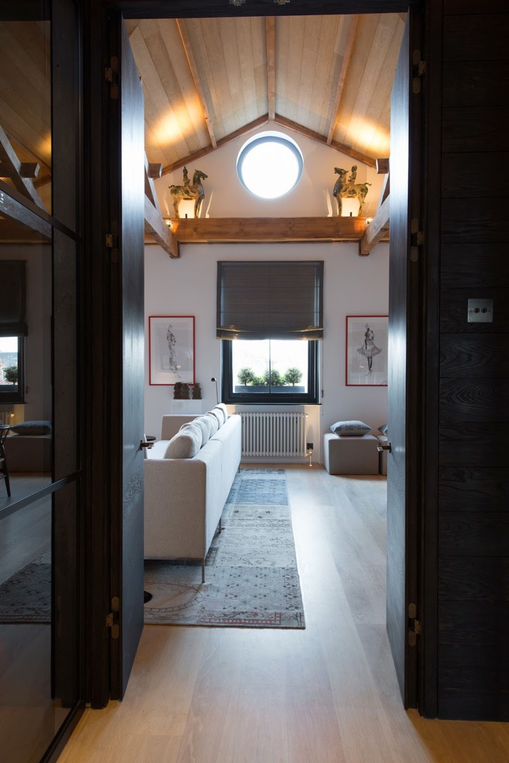 Un interior moderno con techo de madera, tragaluz circular, sofá, radiador y obras de arte enmarcadas.