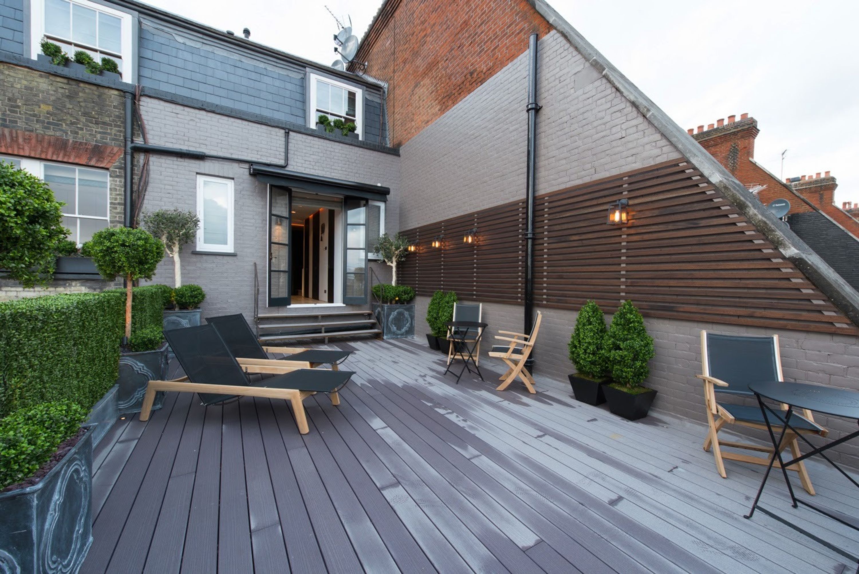 Eine moderne Terrasse mit Holzboden, Sitzgelegenheiten im Freien und einer Backsteinmauer.