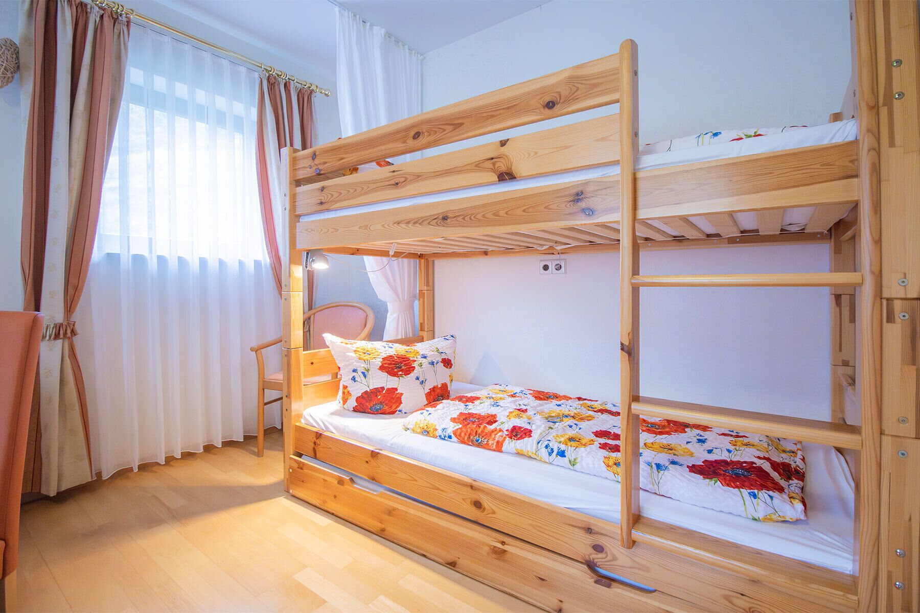 Una cama litera con estructura de madera, una silla y una ventana con cortinas.