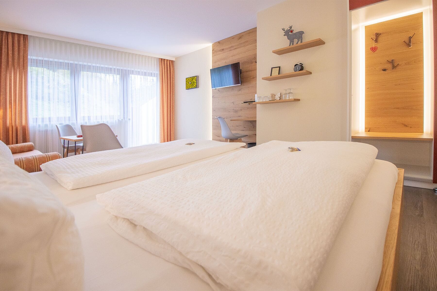 A hotel room with two beds, a TV, a wooden wall, and a window with curtains.