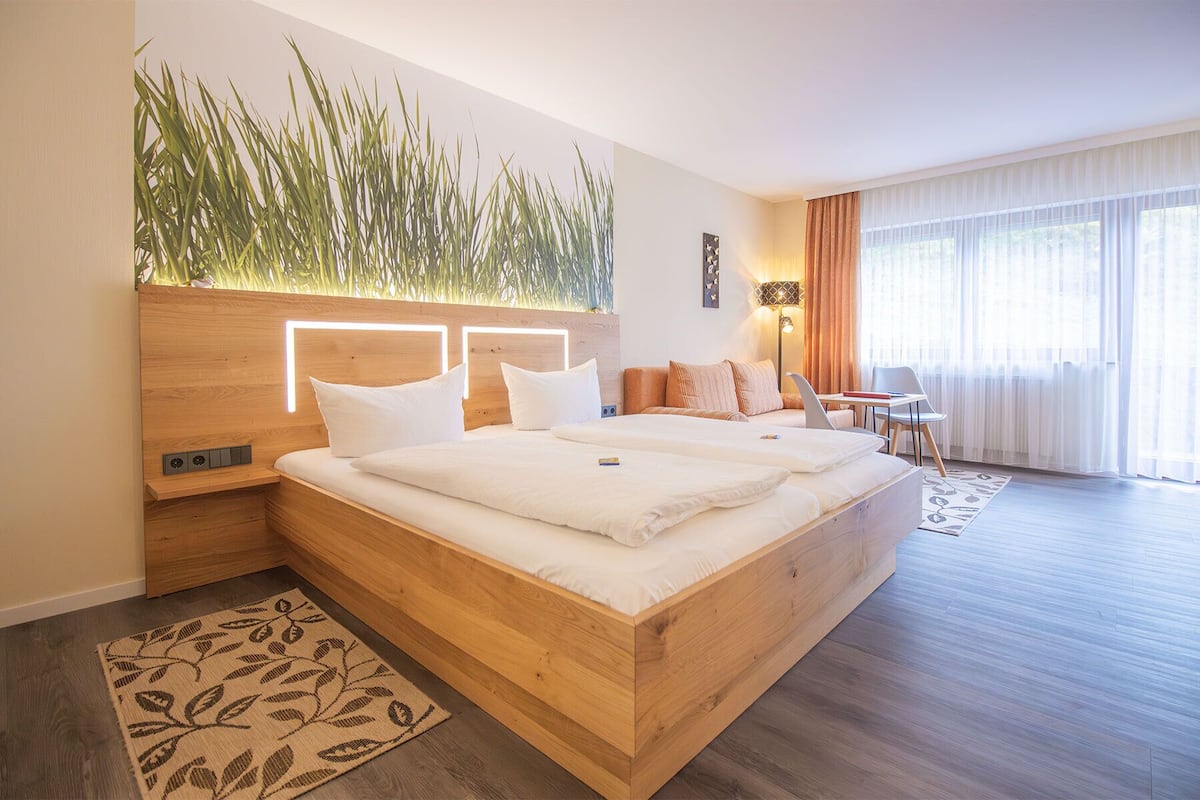 Habitació d'hotel moderna amb llit de fusta, escriptori i finestra gran amb cortines.