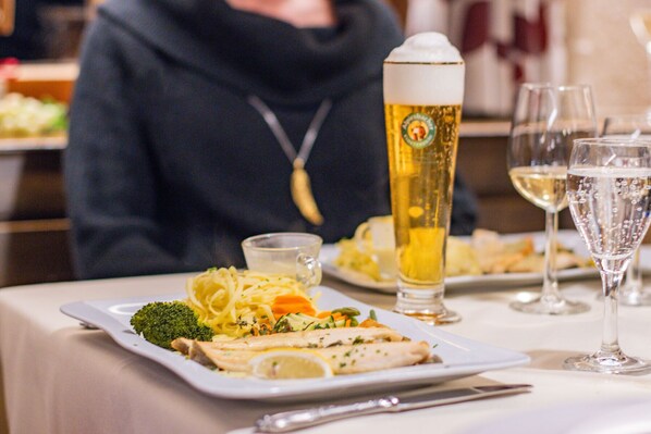 A dining table with a plate of food, a tall beer glass, and a wine glass.