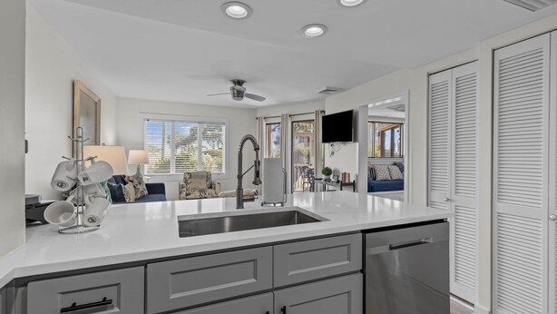 A modern kitchen with a central island, recessed ceiling lights, and a view to a living area with a sofa and a dining table. - Port O' Call D102 - Walkout to Beach/Ocean! (Isle of Palms)