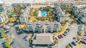 An aerial view of a beachfront hotel with multiple buildings, a swimming pool, and a parking lot. - Port O' Call D102 - Walkout to Beach/Ocean! (Isle of Palms)