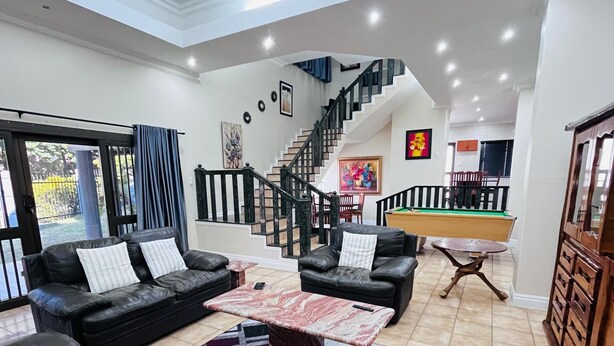 A spacious living room with a black leather sofa, a coffee table, and a staircase leading to an upper level. - Marion guest house (Ballito)