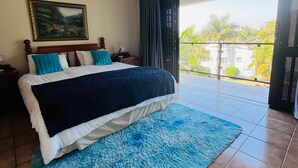 A bedroom with a large bed, a painting on the wall, and a view of the outside through a sliding door. - Marion guest house (Ballito)