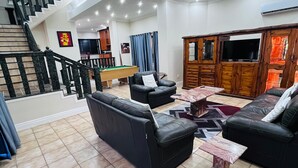 A spacious living room with a pool table, black leather sofas, a TV, and a staircase leading to another level. - Marion guest house (Ballito)
