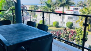 A balcony with a table and chairs, offering a view of a residential area with houses and palm trees. - Marion guest house (Ballito)