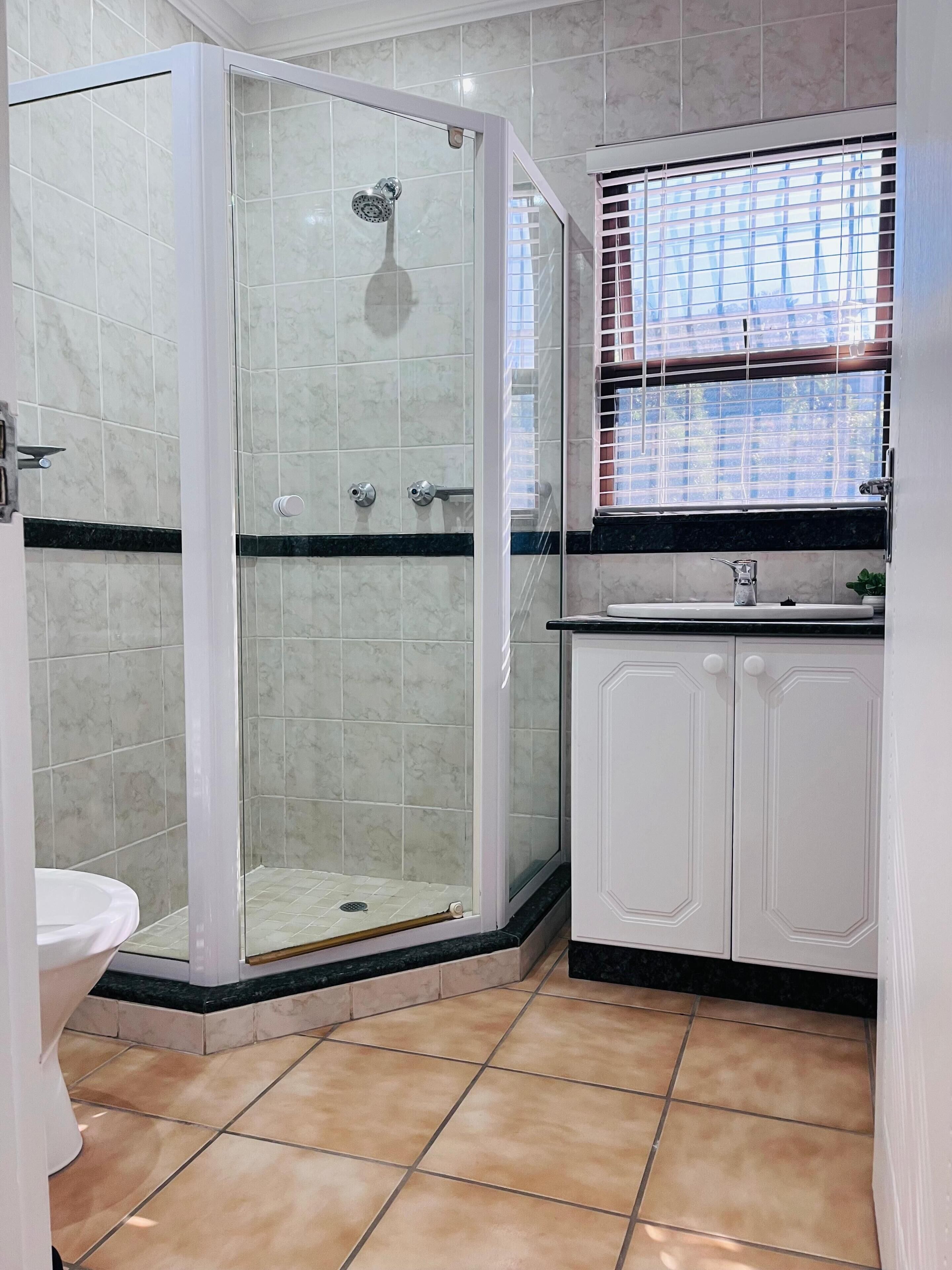 Ein Badezimmer mit einer Duschkabine, einer Toilette und einem Waschbecken mit Fenster darüber.