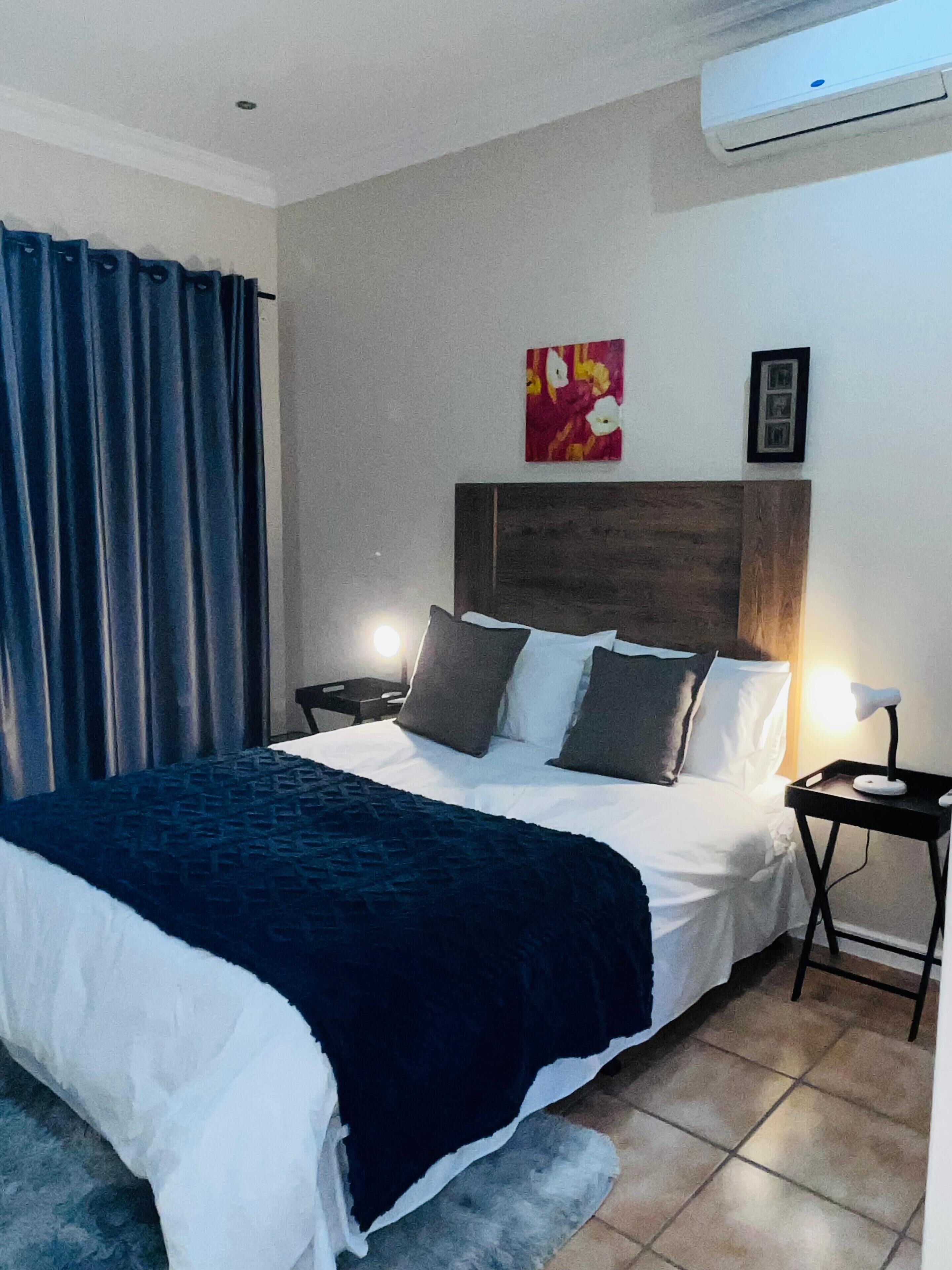Une chambre d’hôtel avec un grand lit, une table de chevet, une lampe, un climatiseur et un tableau au mur.