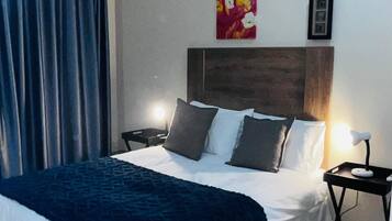 Une chambre d’hôtel avec un grand lit, une table de chevet, une lampe, un climatiseur et un tableau au mur.
