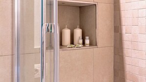 A shower with a glass door, beige tiles, and a shelf with toiletries. - Suite Manzoni by Houset (Monza)