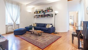 A modern living room with a blue sofa, a coffee table, a bookshelf, and a piano. - Suite Manzoni by Houset (Monza)