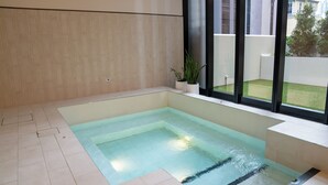 A modern indoor swimming pool with clear water, surrounded by light-colored tiles and a large window. - Home in the Sky 2BR,2BA with City Views,Pool & Gym (Melbourne)