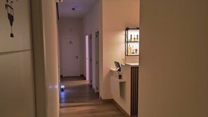 Corredor de hotel com piso de madeira, minibar e porta com o símbolo de uma taça de vinho.