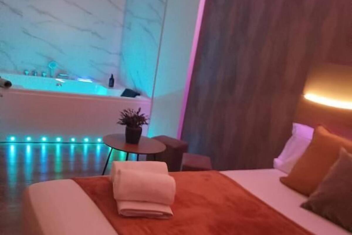 A modern hotel room with a large bed, a small table with a plant, and a view of a bathtub.