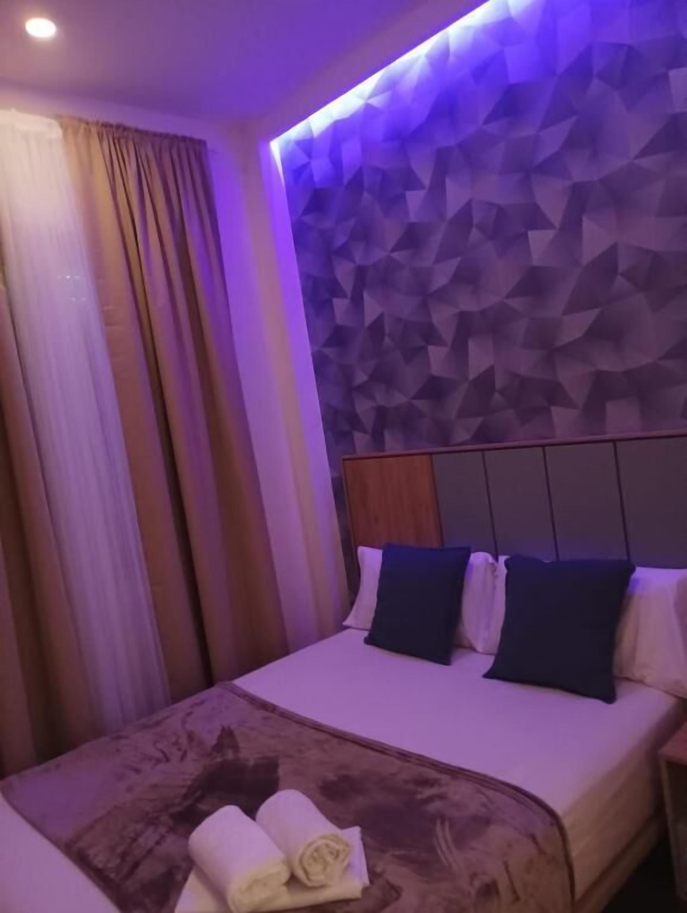 Una habitación de hotel con un cabecero de estampado geométrico, una cama con almohadas blancas y azul oscuro, y una cama bien hecha con toallas enrolladas.