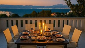 A table set for dinner with multiple dishes and glasses of wine, overlooking a body of water and distant cityscape. - Caecilia Lawrence Bio Sea Villa - Sleeps 12 (Chalcis)