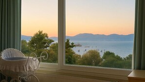 A room with a view of a lake and mountains, a window with curtains, and a baby stroller. - Caecilia Lawrence Bio Sea Villa - Sleeps 12 (Chalcis)