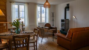 Un salon chaleureux avec un plancher en bois, un canapé en cuir marron, une table à manger avec des chaises et une grande fenêtre.