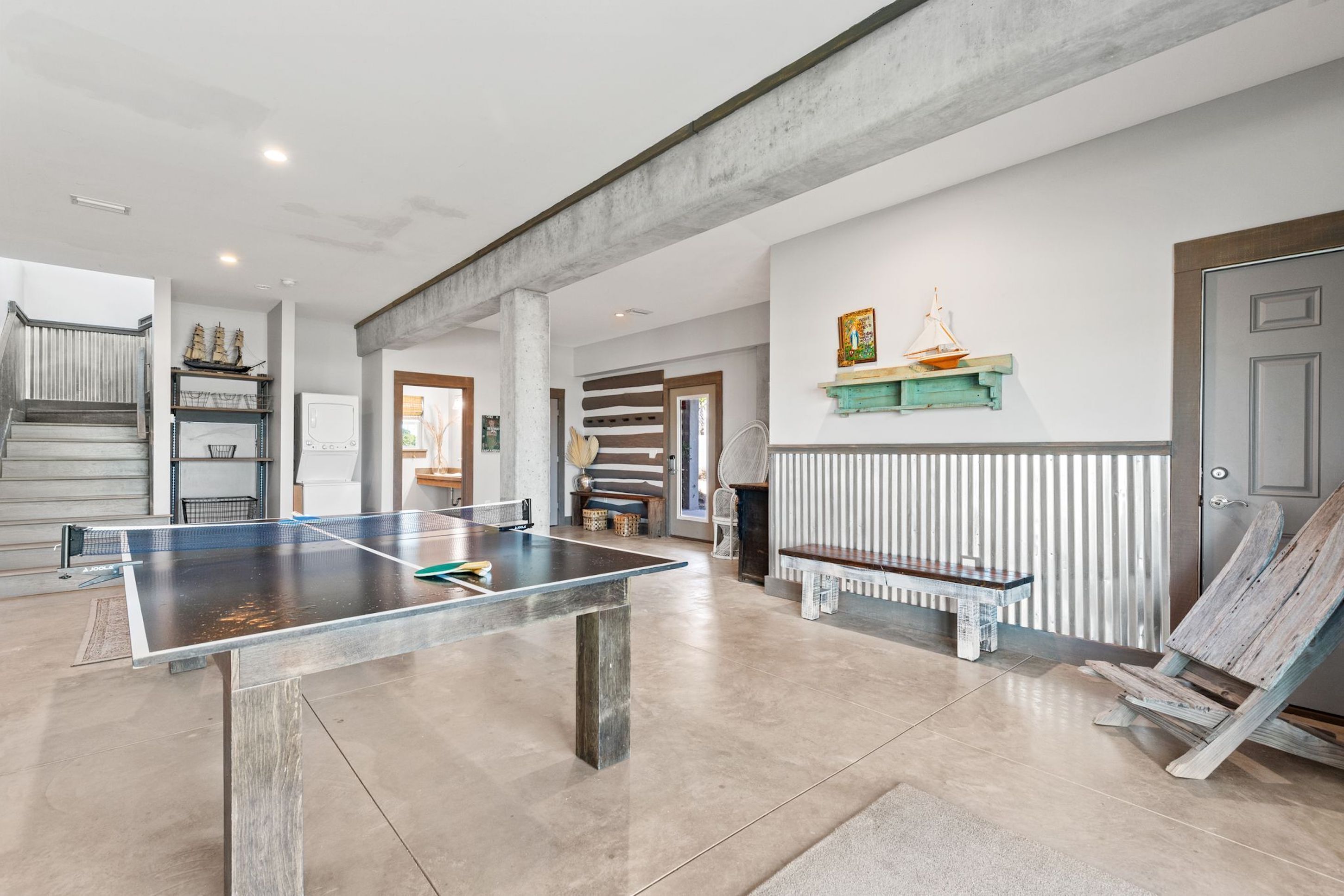 A spacious room with a ping pong table, a wooden bench, and a staircase leading to another level.