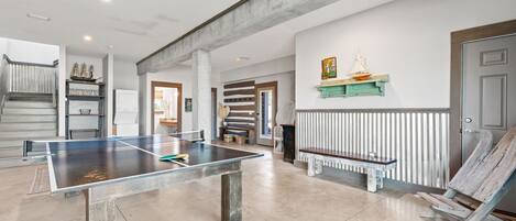 A spacious room with a ping pong table, a wooden bench, and a staircase leading to another level.