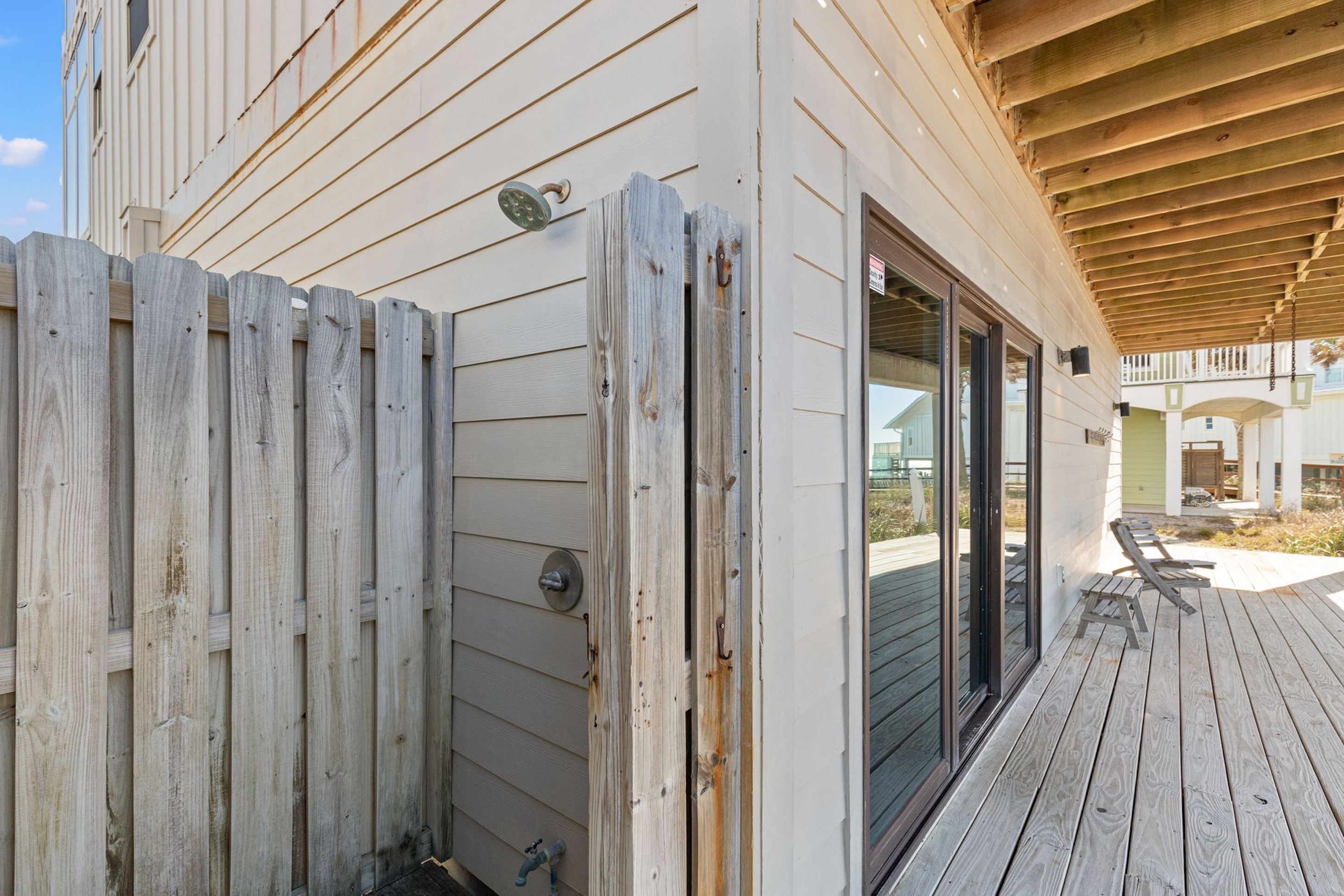 A wooden deck with a wooden fence, a sliding glass door, and a covered patio area.