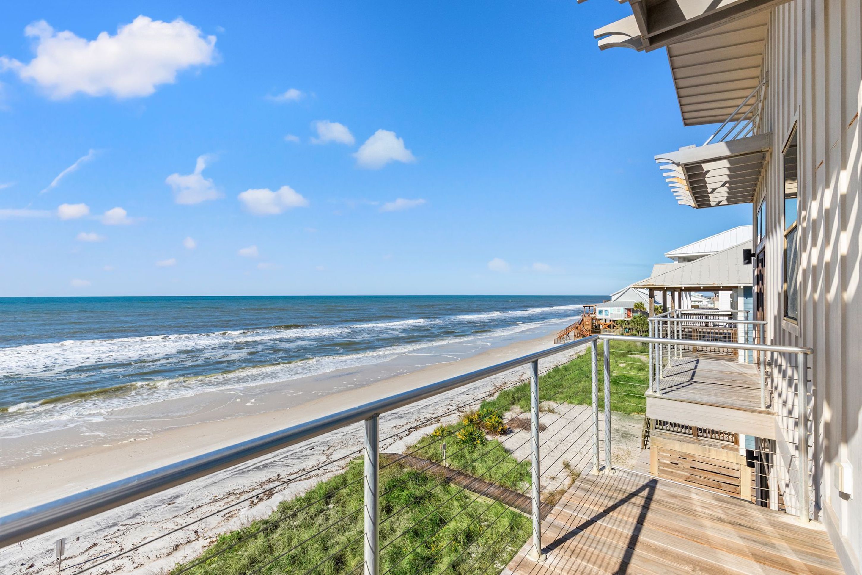 A beachfront property with a wooden deck and a balcony overlooking the ocean.