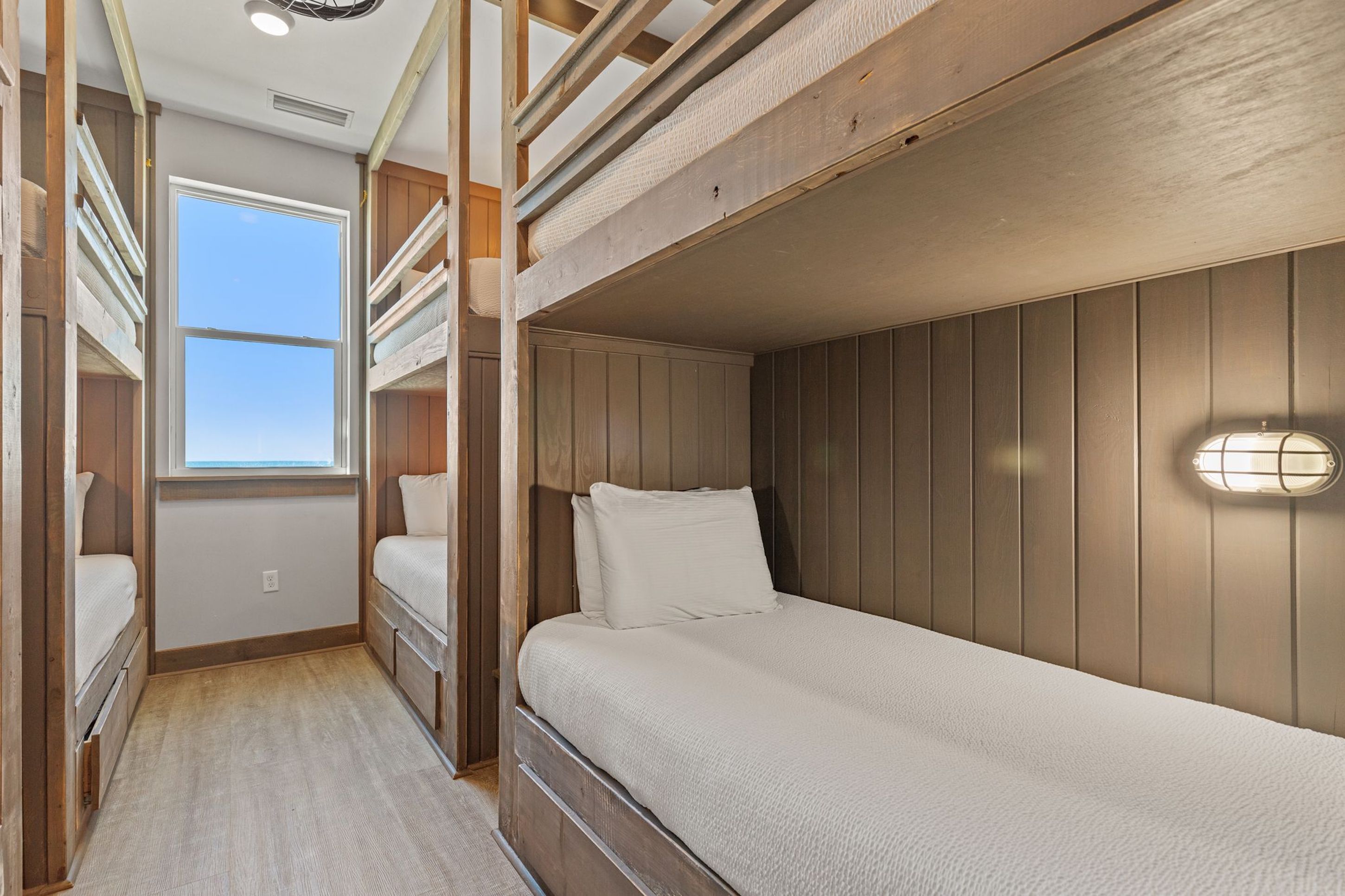A bunk bed room with a window, wooden walls, and a light fixture.