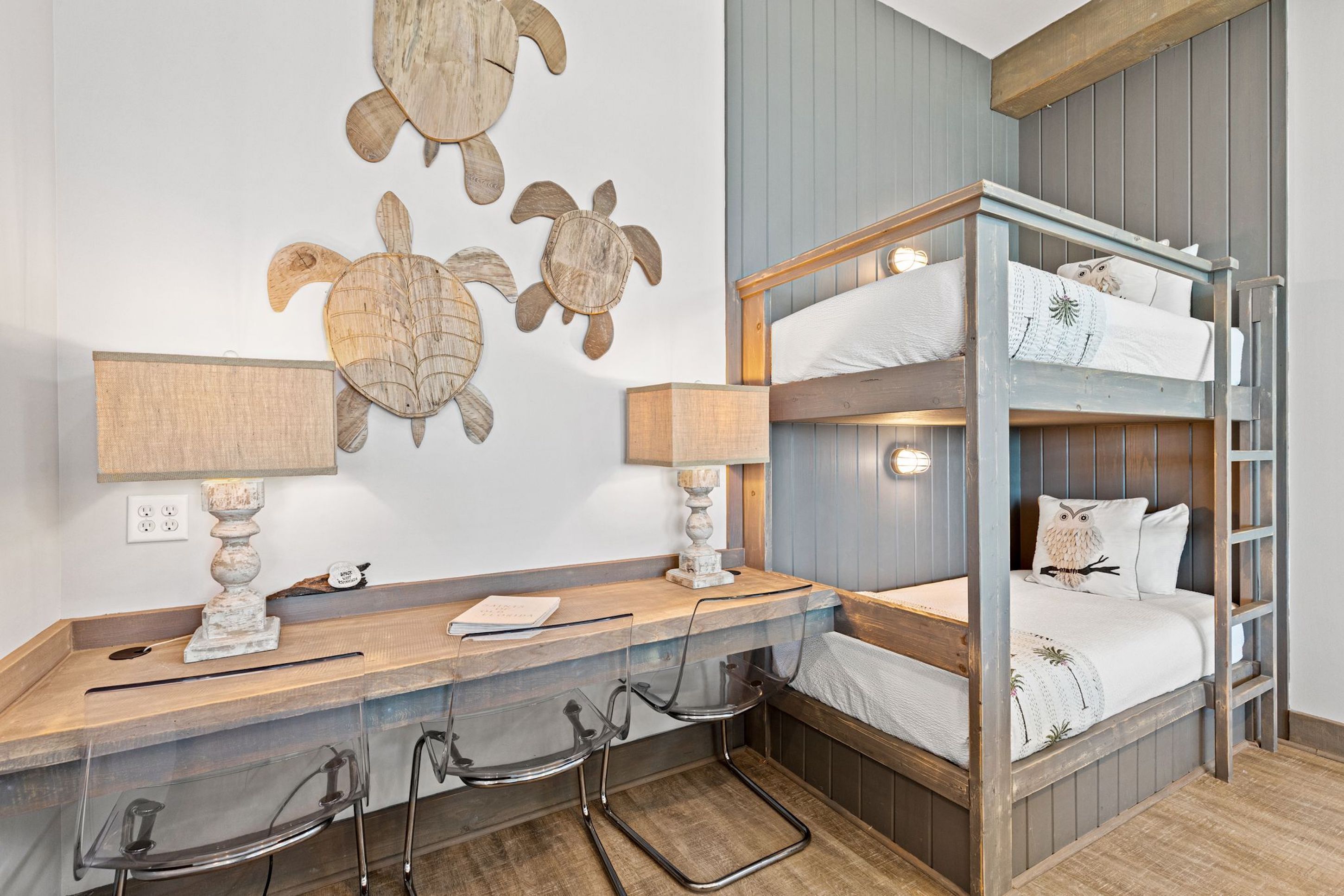 Un lit superposé avec une structure en bois et une literie blanche, un bureau avec une lampe et des décorations murales représentant des tortues.