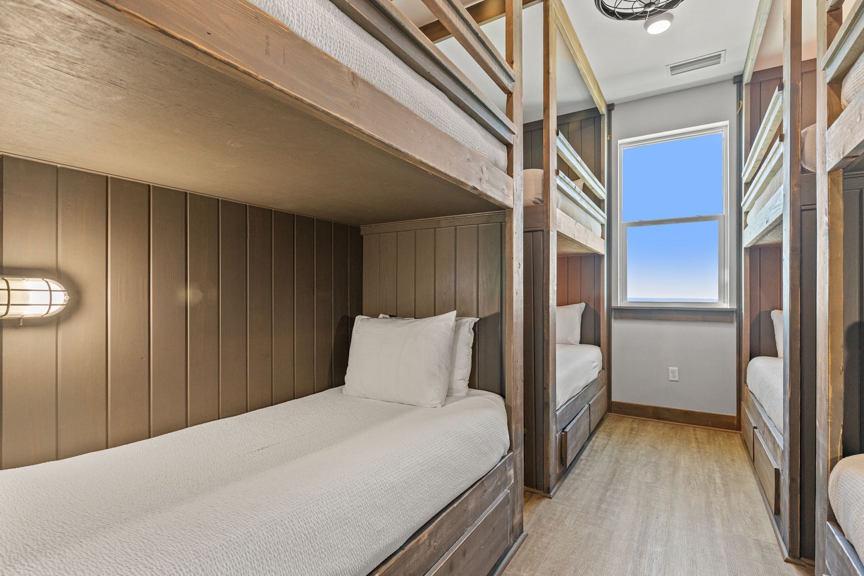 A bunk bed room with a window, wooden walls, and a light fixture.