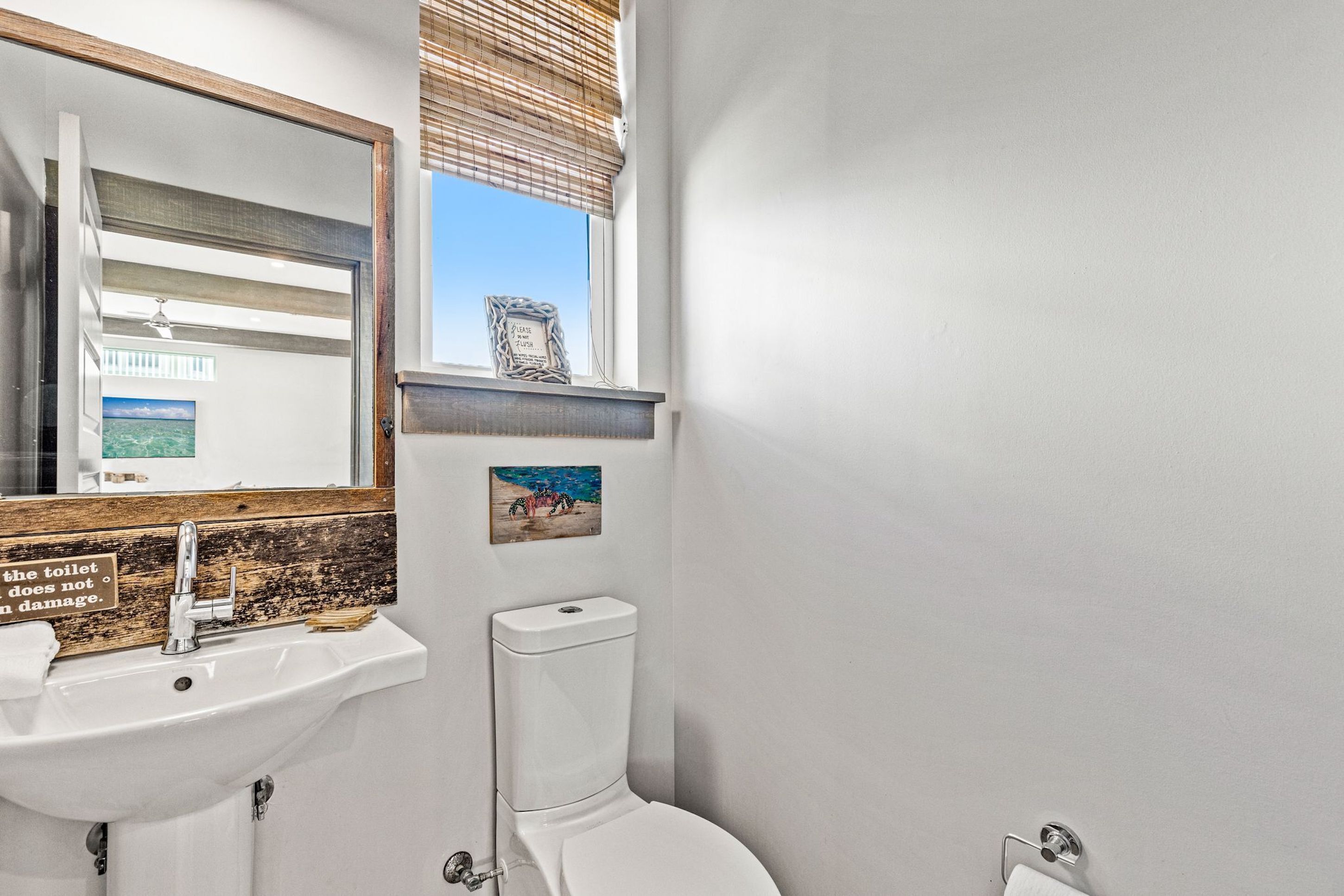Un baño con lavamanos blanco, un espejo, inodoro y ventana con persianas.