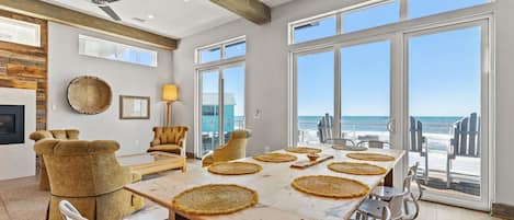 Un vaste espace dédié à la salle à manger, avec une grande table, des chaises et une vue sur l’océan grâce à de grandes fenêtres.