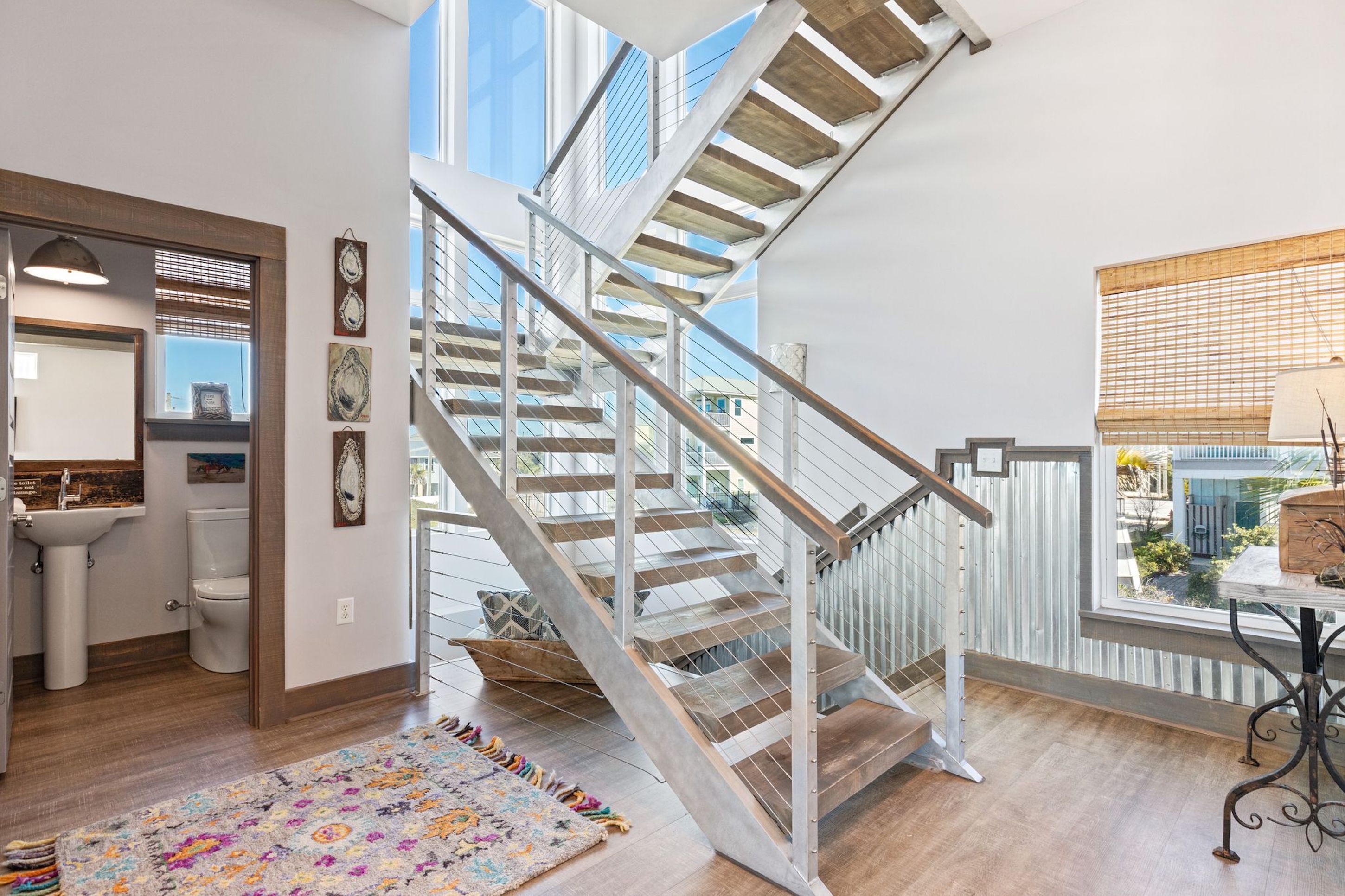 A modern interior with a wooden staircase, a bathroom with a sink and toilet, and a view through a large window.