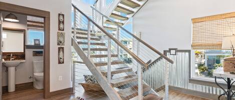 A modern interior with a wooden staircase, a bathroom with a sink and toilet, and a view through a large window.