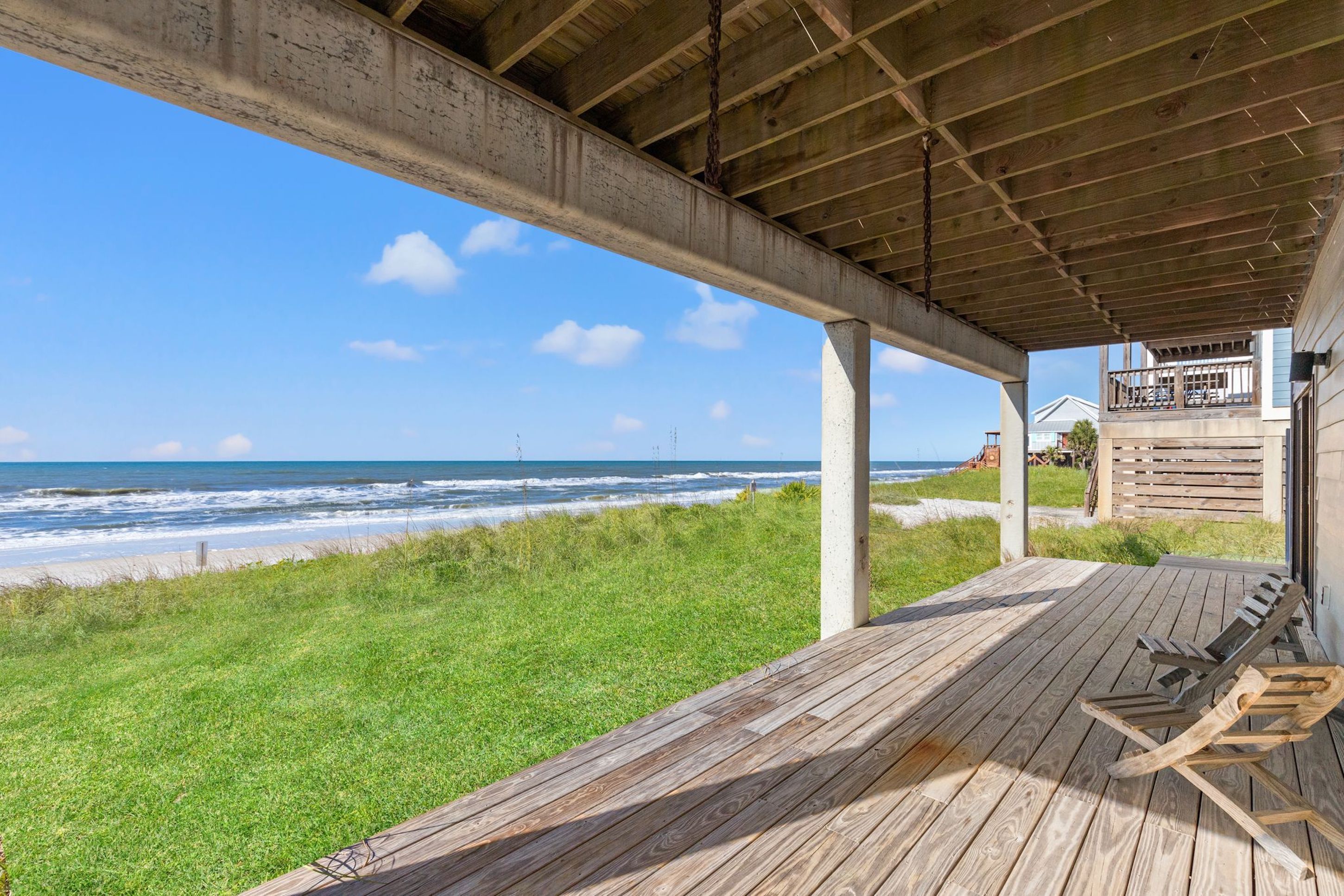 A wooden deck with a view of the ocean, a covered area with a railing, and a building in the background.