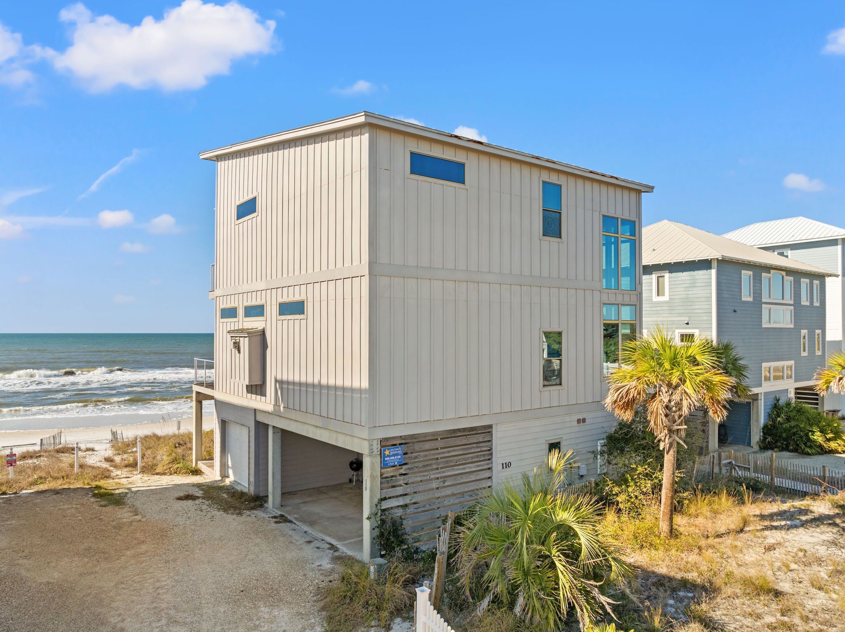 A two-story beach house with a garage, a balcony, and a view of the ocean.