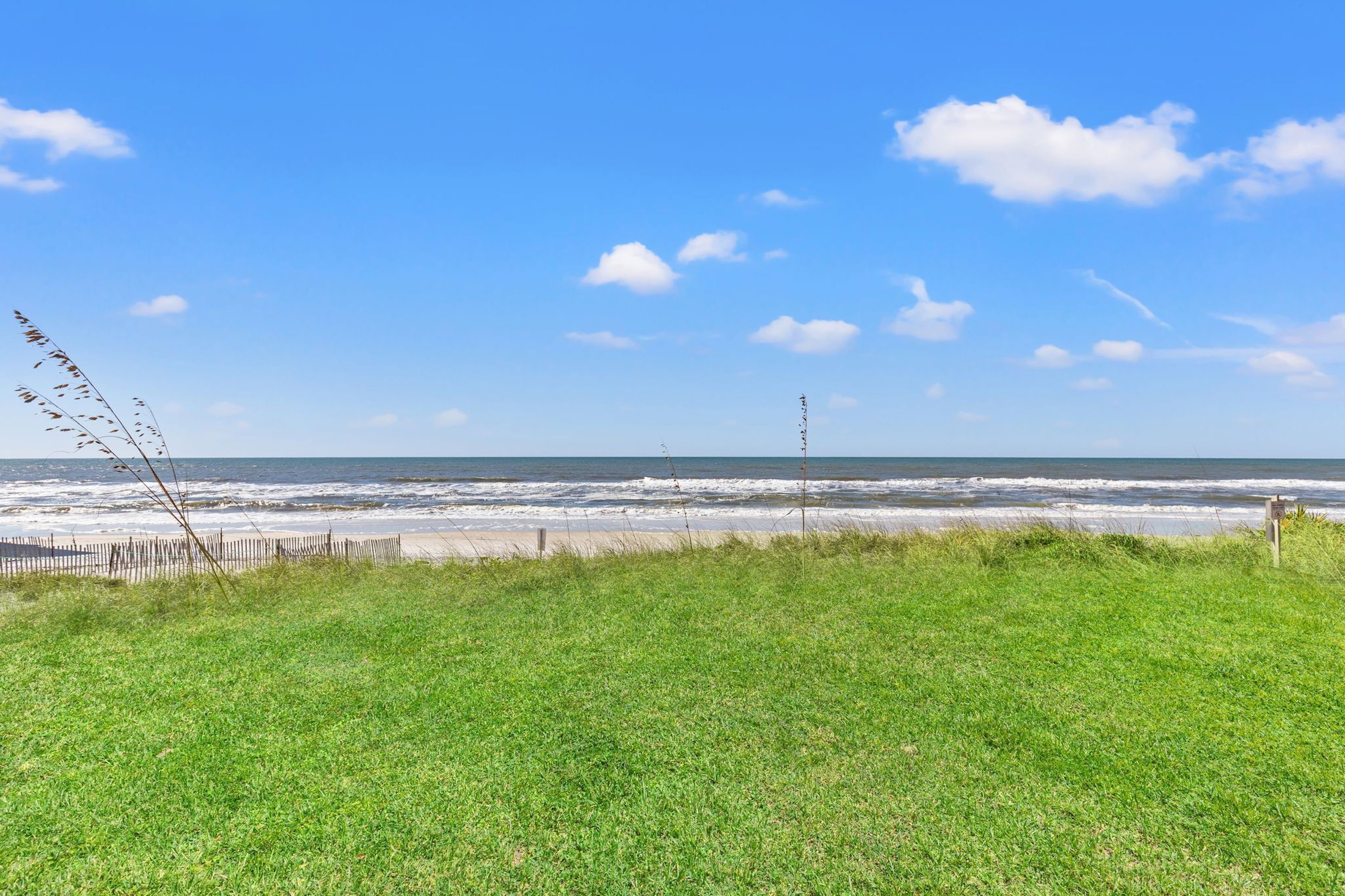 Una spiaggia erbosa con una recinzione in legno e una vista libera sull'oceano.