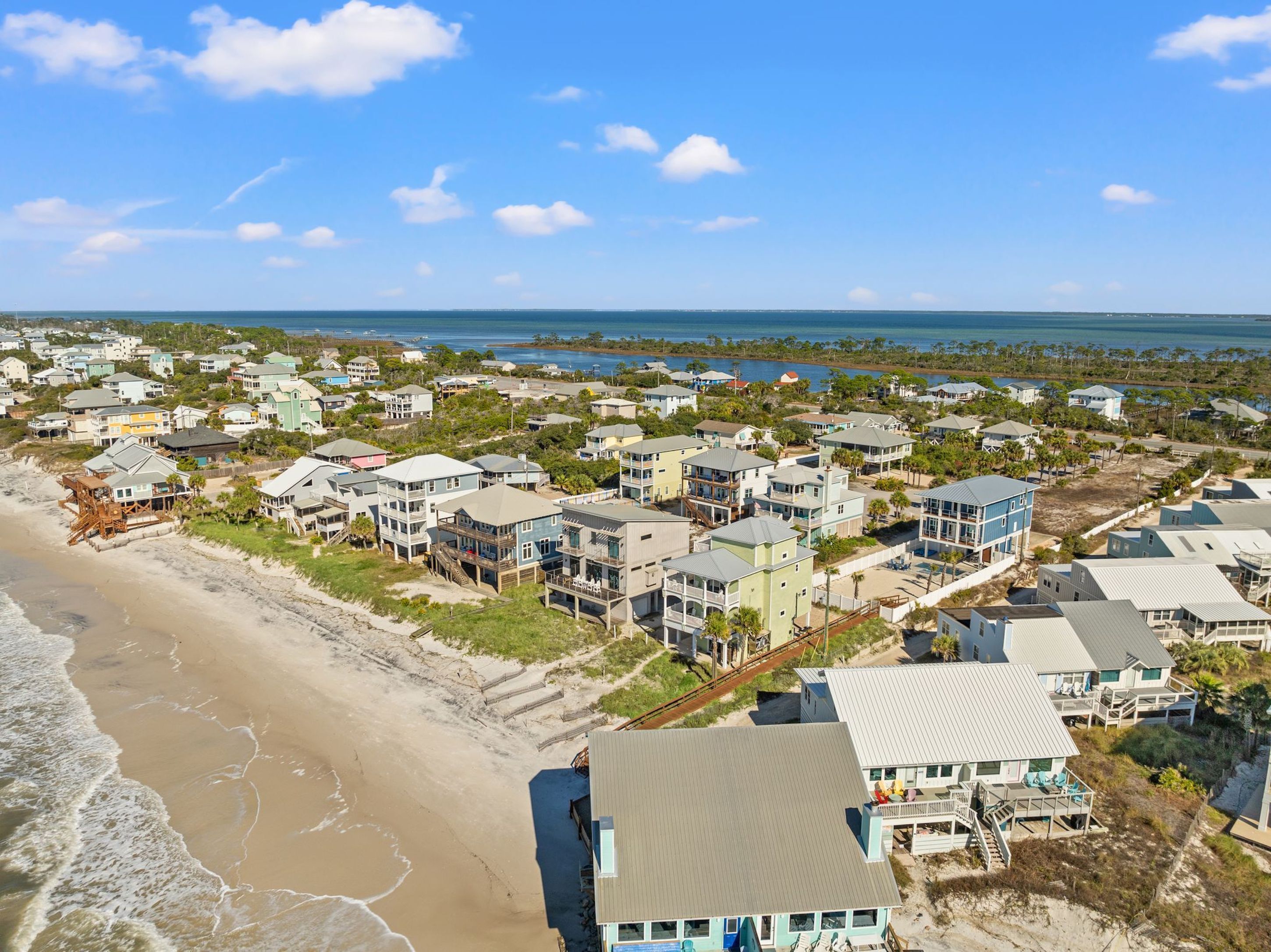 Un quartier résidentiel situé sur la côte, avec des propriétés donnant sur la plage, notamment des maisons dotées de balcons et de terrasses, et une plage en premier plan.