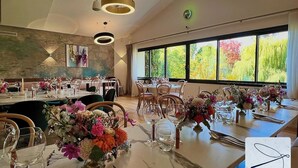 Un restaurante con varias mesas dispuestas para comensales, con centros de mesa florales y cristalería transparente.