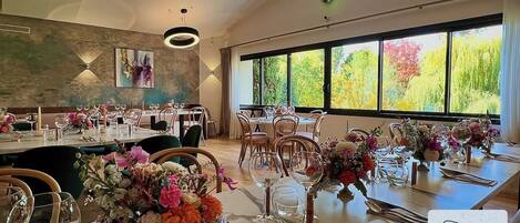 A restaurant with multiple dining tables set for guests, featuring floral centerpieces and clear glassware.